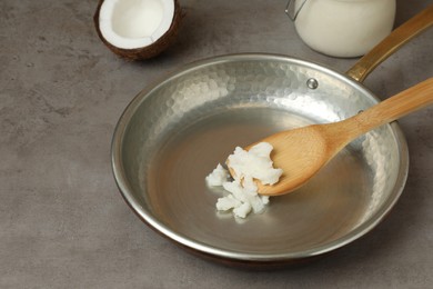 Photo of Frying pan with coconut oil and wooden spatula on grey table. Healthy cooking