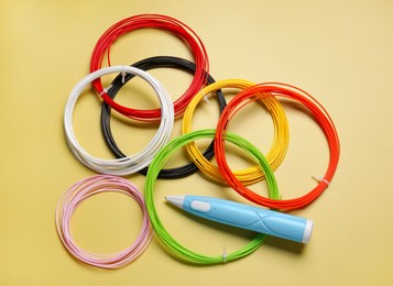 Photo of Stylish 3D pen and colorful plastic filaments on yellow background, flat lay