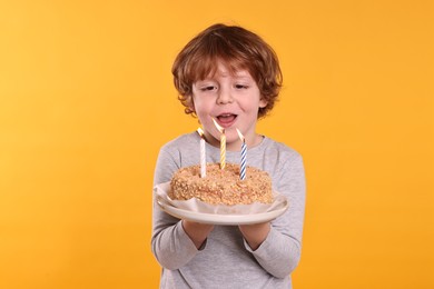 Photo of Birthday celebration. Cute little boy holding tasty cake with burning candles on orange background
