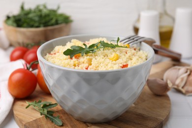 Photo of Bowl of tasty couscous with pepper, corn, arugula and fork on white table, closeup