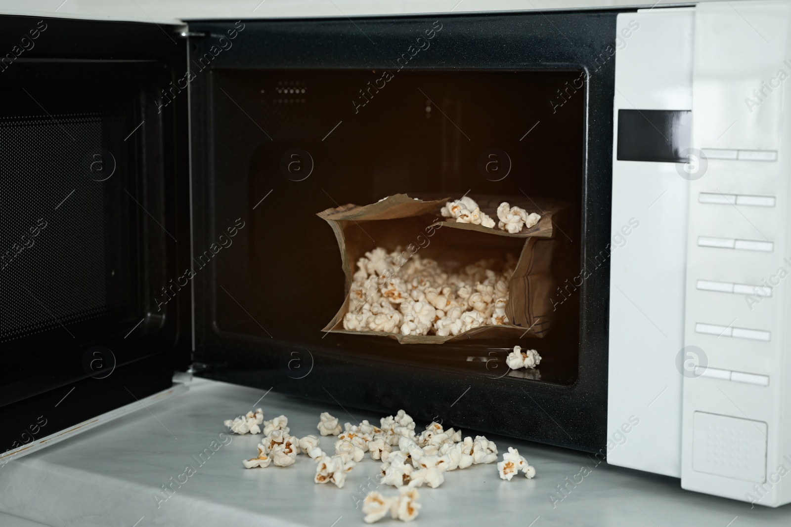 Photo of Open microwave oven with fresh popcorn on table