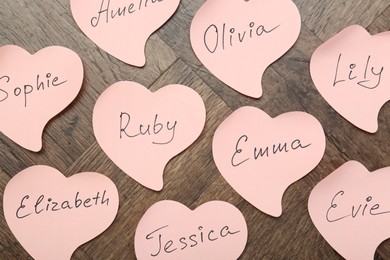 Paper stickers with different names on wooden background, flat lay. Choosing baby's name