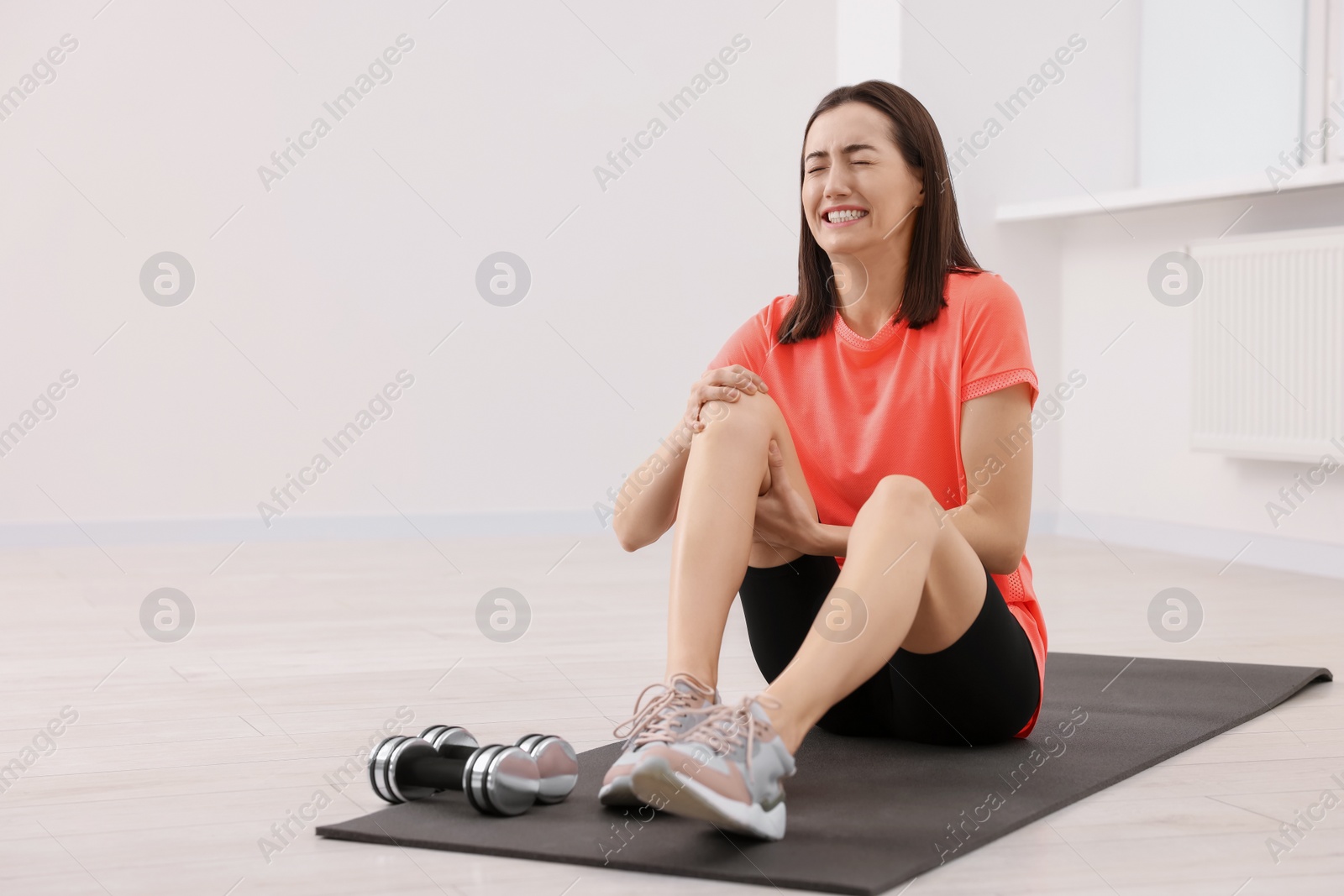 Photo of Young woman suffering from leg pain on exercise mat indoors, space for text