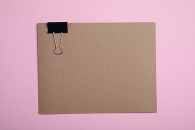 Photo of Sheet of brown paper with clip on pink background, top view