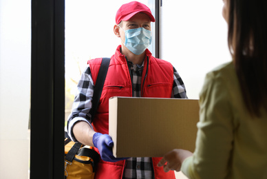Photo of Courier giving cardboard box to woman at entrance. Delivery service during coronavirus quarantine