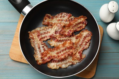 Photo of Delicious bacon slices in frying pan on blue wooden table, flat lay