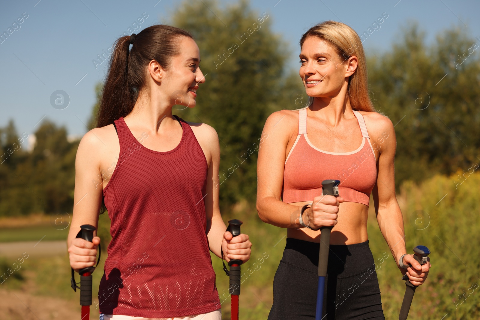 Photo of Happy women practicing Nordic walking with poles outdoors on sunny day