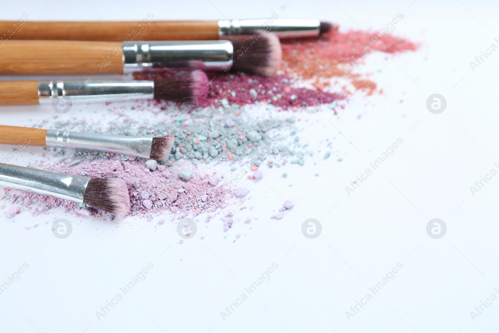 Photo of Different makeup brushes with crushed cosmetic products on light background. Space for text