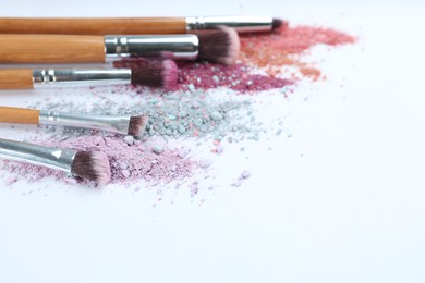 Different makeup brushes with crushed cosmetic products on light background. Space for text