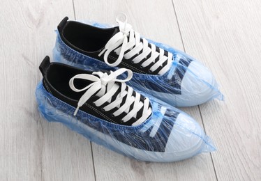 Photo of Sneakers in blue shoe covers on light wooden floor