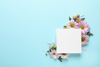 Beautiful chamomile flowers and paper card on color background, flat lay with space for text