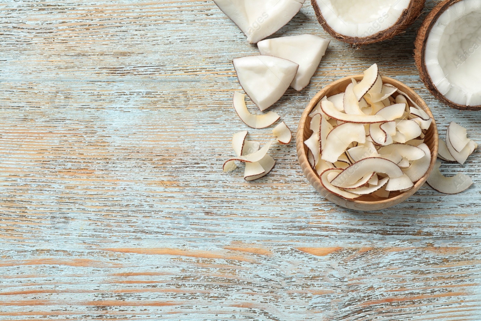 Photo of Flat lay composition with tasty coconut chips on light blue wooden table. Space for text