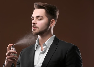 Photo of Handsome man in suit using perfume on dark background