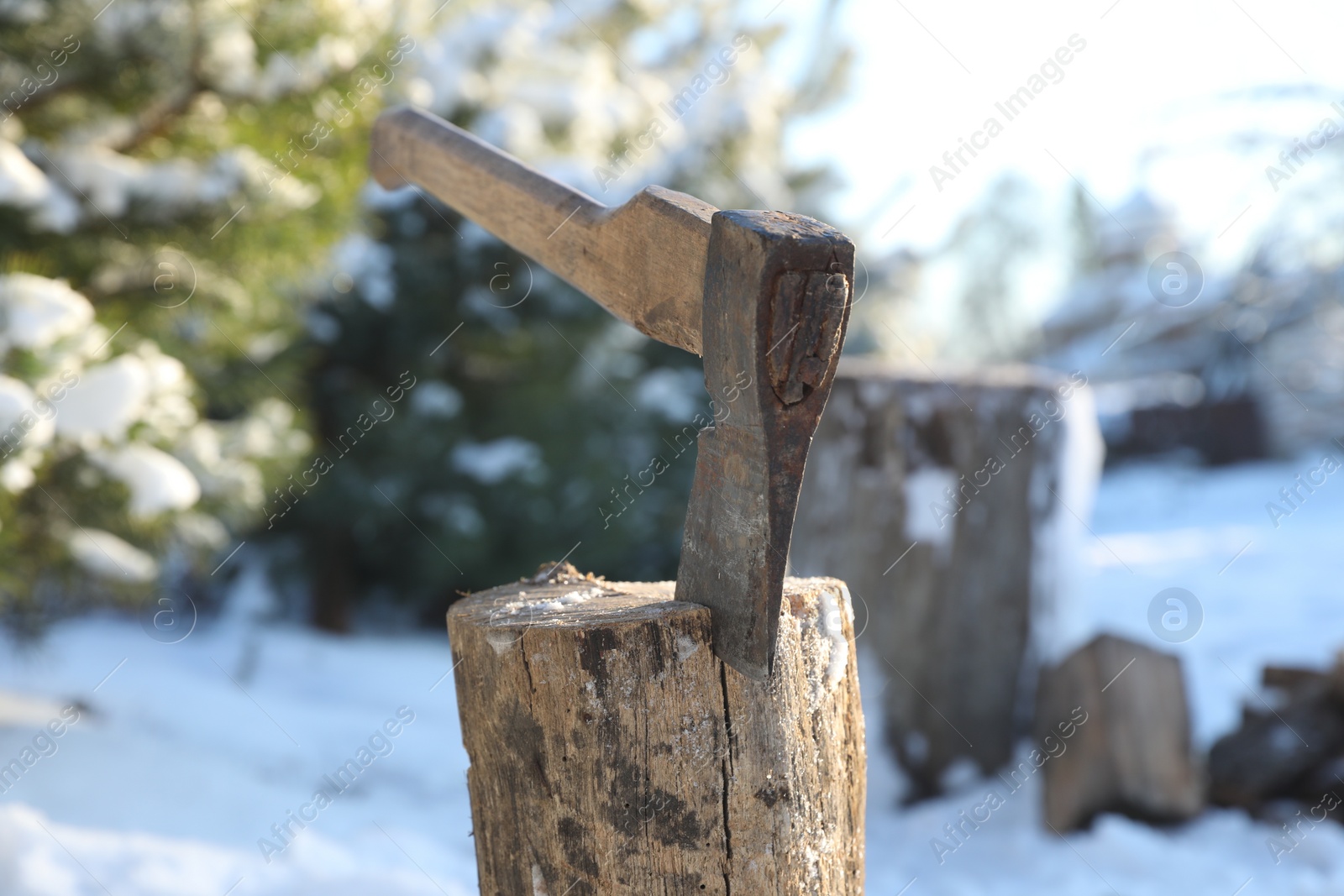 Photo of Metal axe in wooden log outdoors on sunny winter day