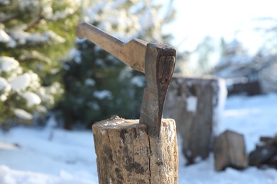 Metal axe in wooden log outdoors on sunny winter day