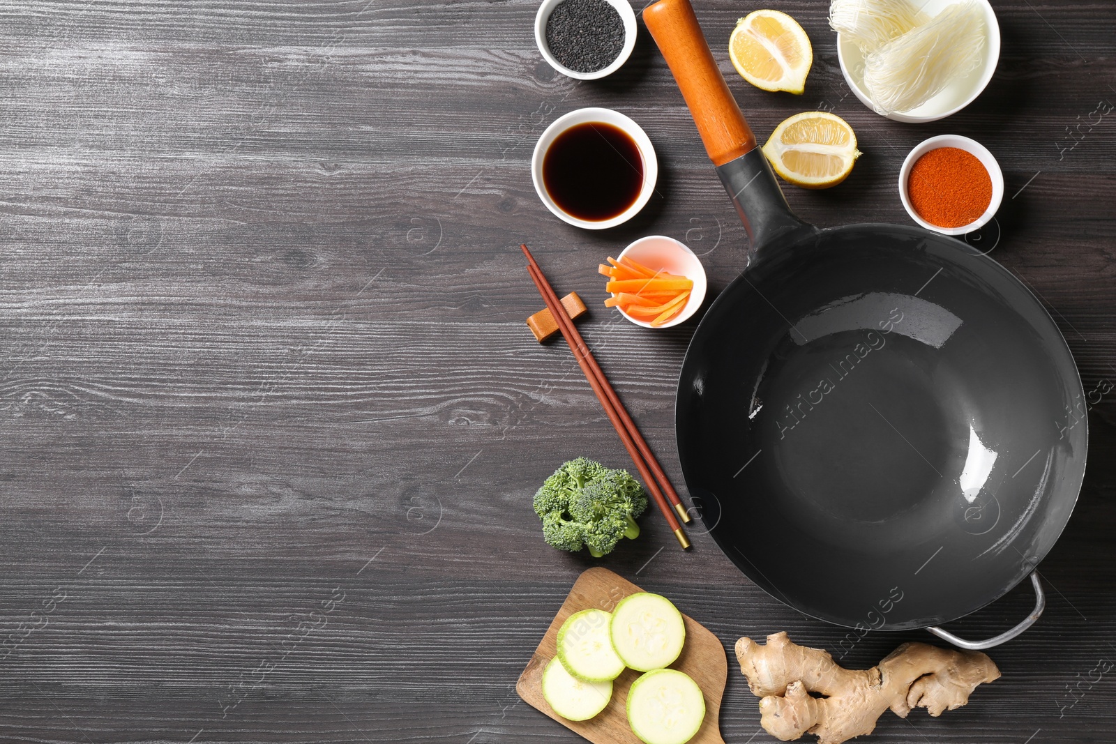 Photo of Empty iron wok, chopsticks and ingredients on grey wooden table, flat lay. Space for text