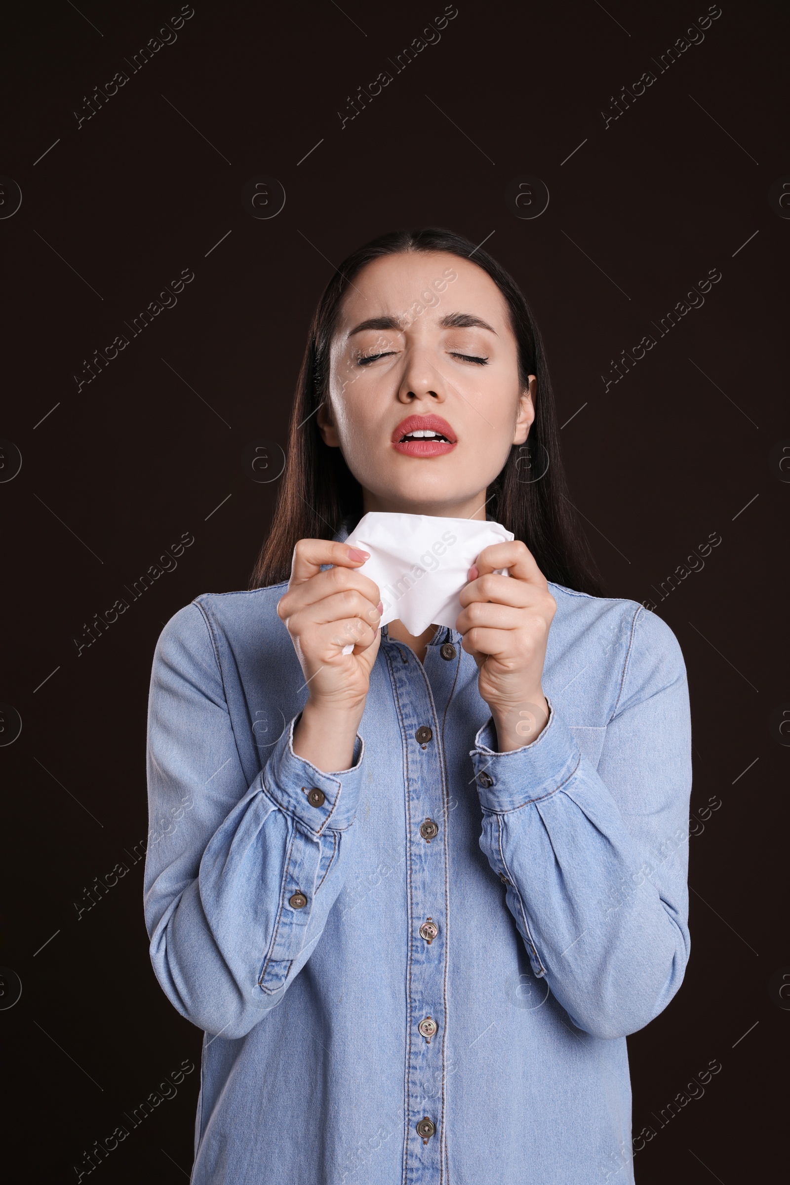 Photo of Sick young woman sneezing in tissue on dark background. Cold symptoms