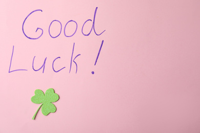 Photo of Phrase GOOD LUCK and clover leaf on pink background, top view. Space for text