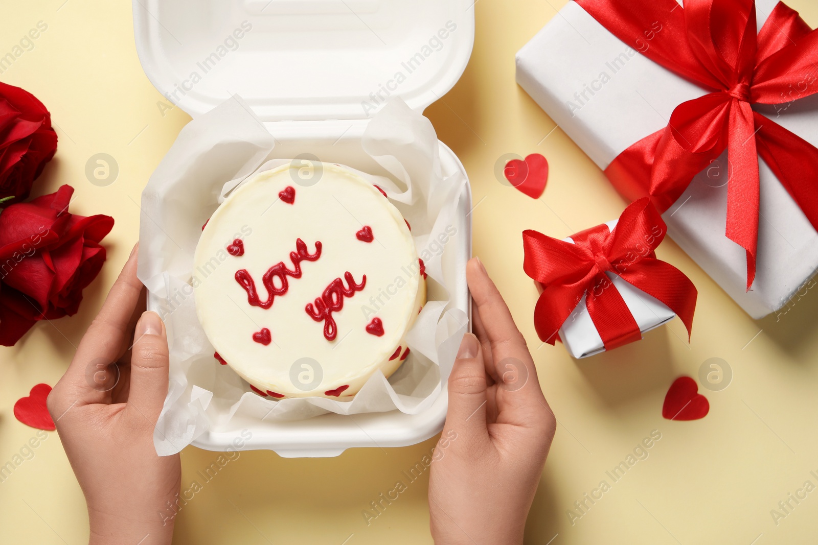 Photo of Woman holding takeaway box with bento cake at beige table, top view. St. Valentine's day surprise