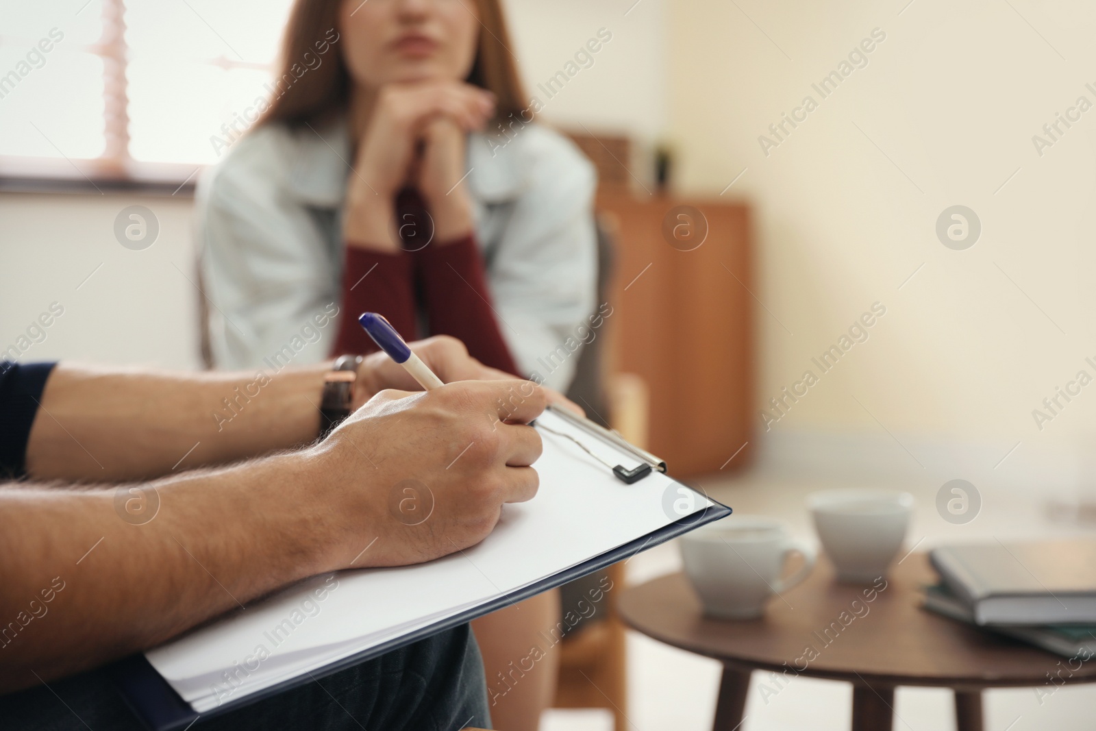 Photo of Professional psychotherapist and patient in office, focus on hands with clipboard