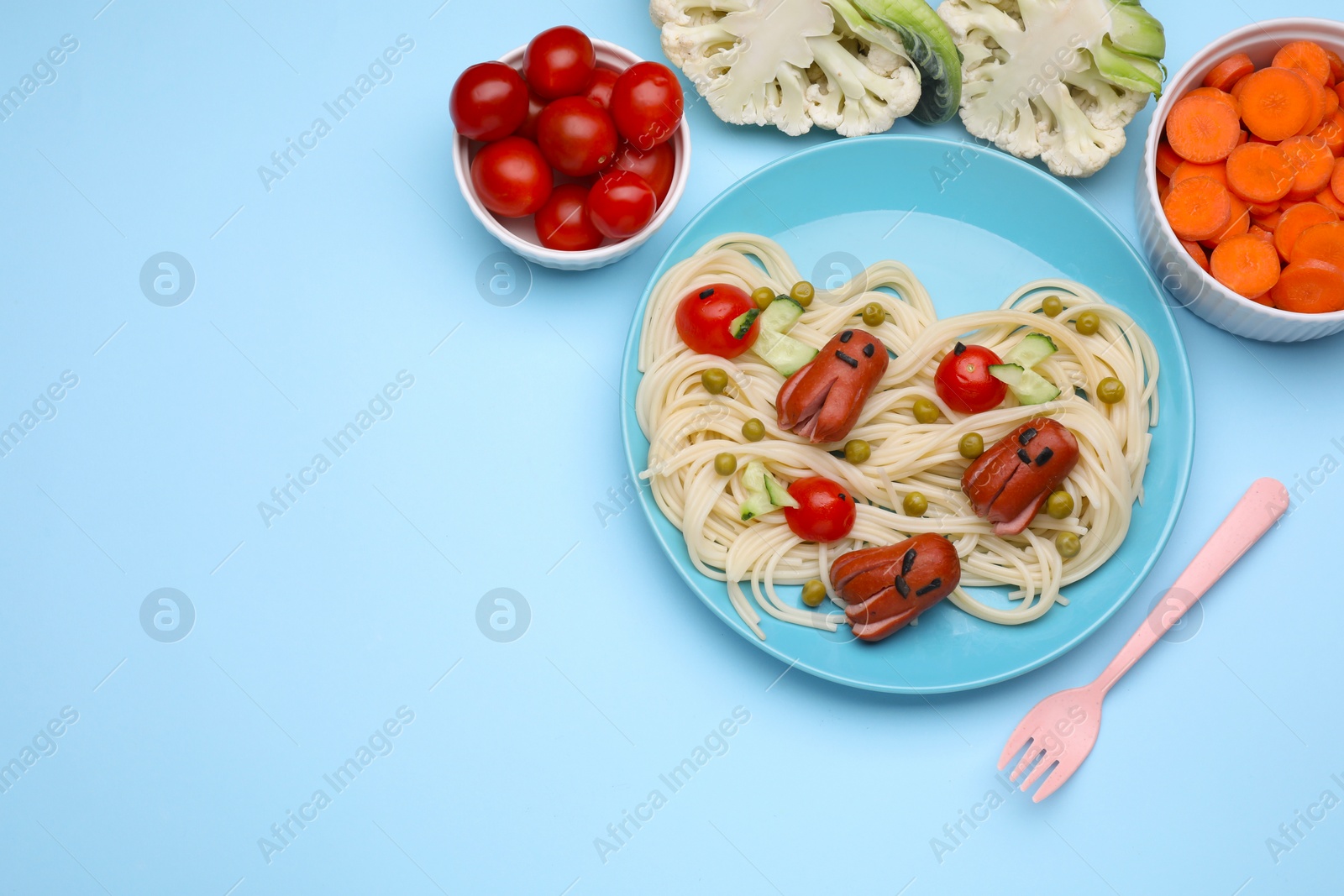 Photo of Creative serving for kids. Plate with cute octopuses made of sausages, pasta and vegetables on light blue table, flat lay. Space for text