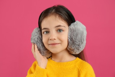 Photo of Cute little girl wearing stylish earmuffs on pink background