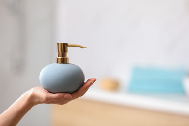 Photo of Woman holding soap dispenser on blurred background, closeup. Space for text