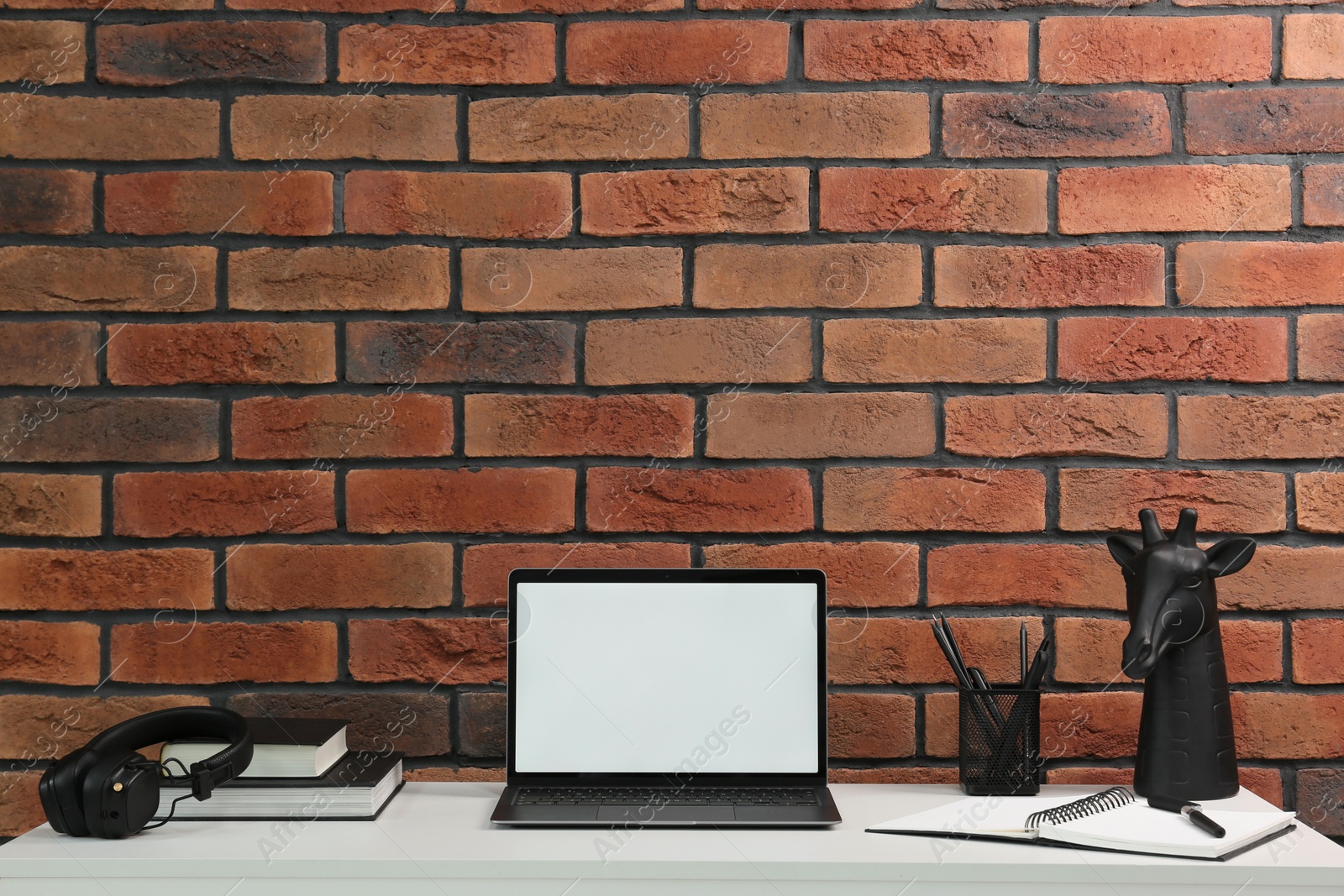 Photo of Stylish workplace with laptop, headphones, stationary and decor on white table near brick wall