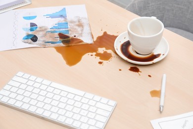 Photo of Cup with saucer and coffee spill on wooden office desk