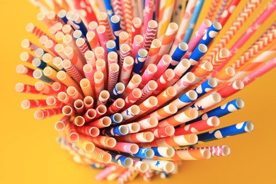 Many paper drinking straws on orange background, closeup