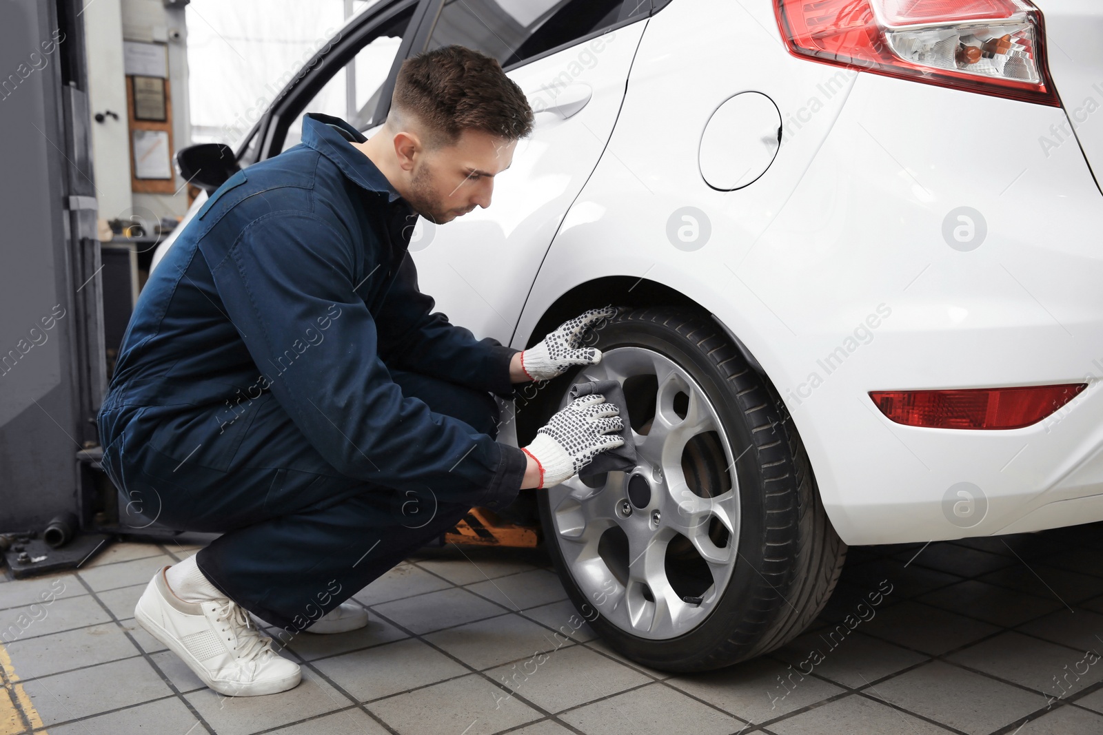 Photo of Young mechanic cleaning wheel at tire service