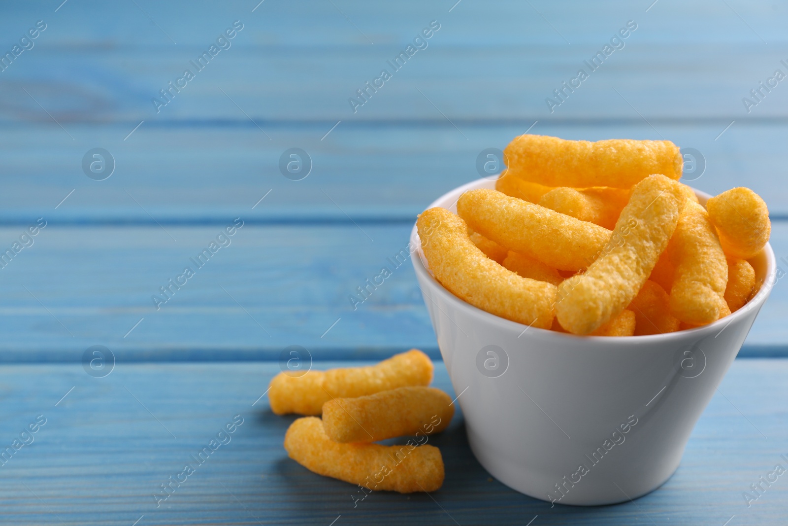 Photo of Many tasty cheesy corn puffs on blue wooden table, space for text