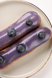 Photo of Delicious eclairs decorated with blueberries on white background, top view