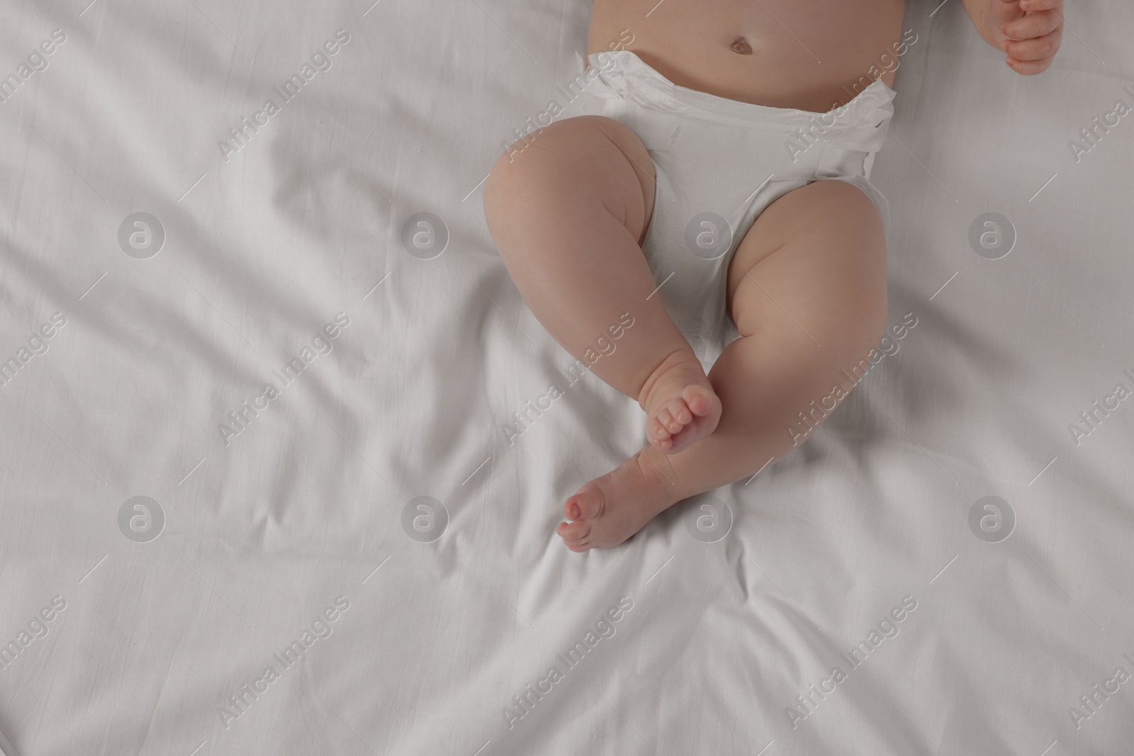 Photo of Little baby in diaper lying on bed, top view