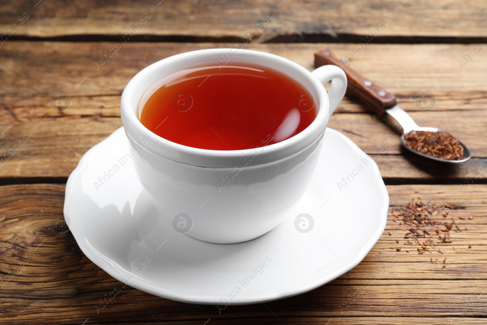 Photo of Freshly brewed rooibos tea, dry leaves and spoon on wooden table