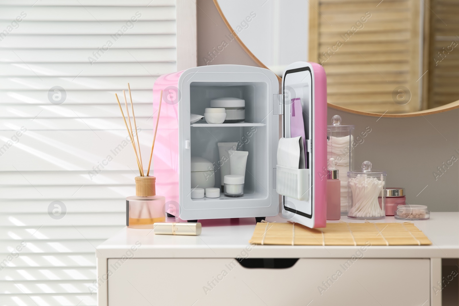 Photo of Cosmetics refrigerator and skin care products on white vanity table indoors