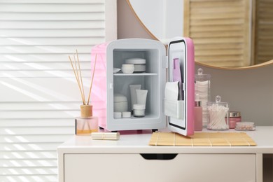 Photo of Cosmetics refrigerator and skin care products on white vanity table indoors