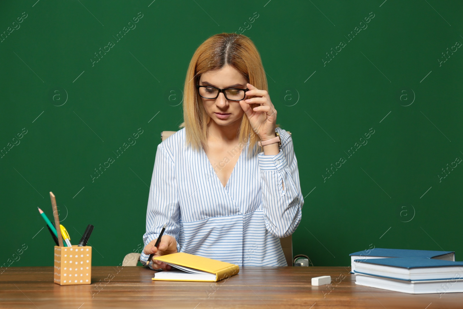 Photo of Portrait of beautiful teacher sitting at table near chalkboard