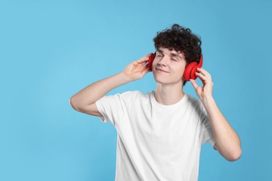 Teenage boy listening music with headphones on light blue background. Space for text