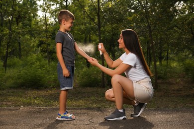 Photo of Woman applying insect repellent on her son's arm in park. Tick bites prevention
