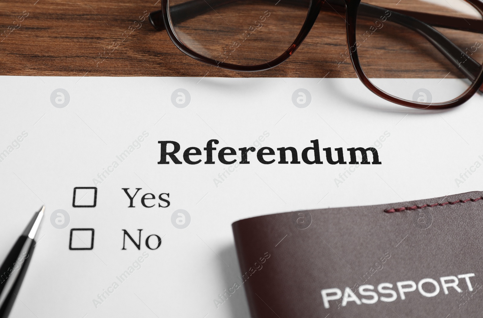 Photo of Referendum ballot with pen, passport and glasses on wooden table, closeup