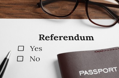 Photo of Referendum ballot with pen, passport and glasses on wooden table, closeup