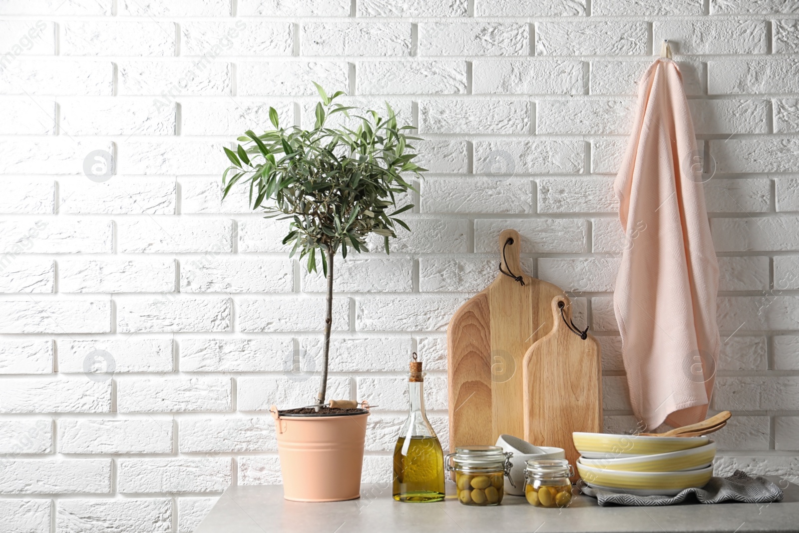 Photo of Fresh oil, olives and kitchen utensils on table near brick wall