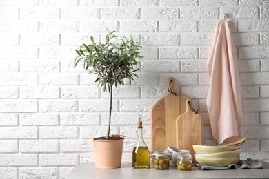 Fresh oil, olives and kitchen utensils on table near brick wall