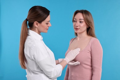 Mammologist checking woman's breast on light blue background