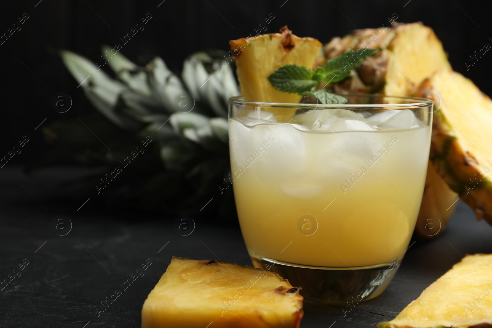 Photo of Delicious fresh pineapple juice with mint and ice cubes on black table, closeup