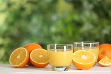 Photo of Delicious orange juice and fresh fruits on wooden table against blurred background. Space for text