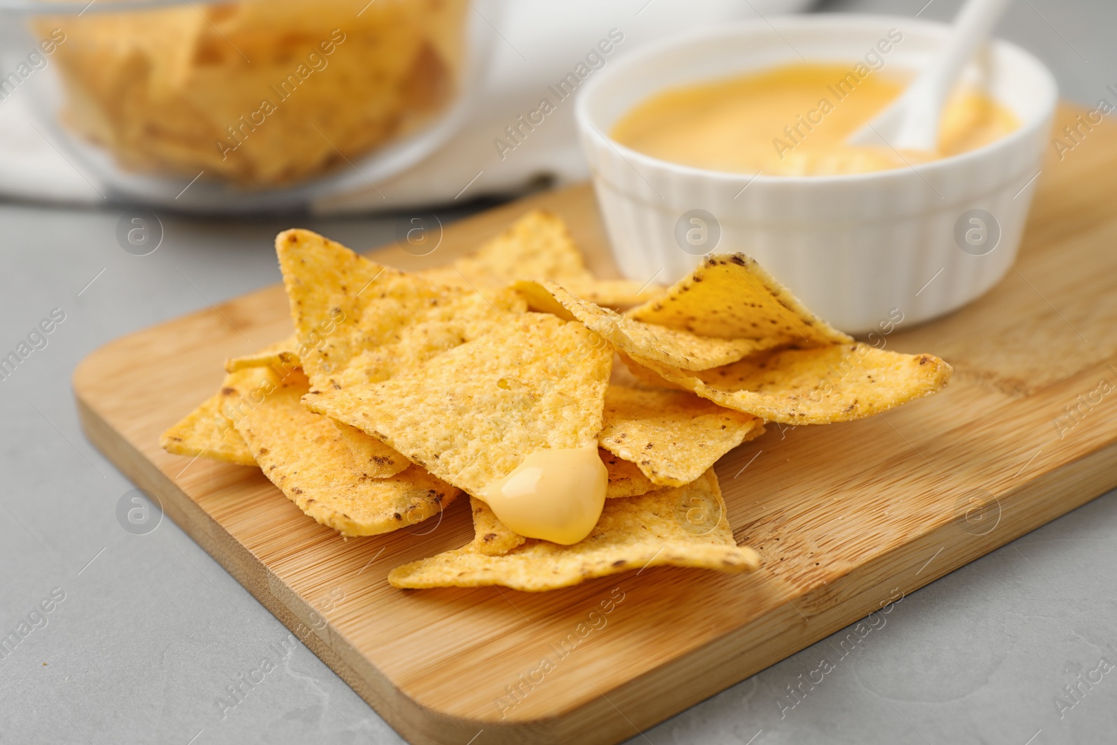 Photo of Board with Mexican nacho chips and sauce on grey table, closeup