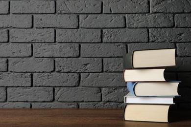 Stack of hardcover books on wooden table near dark brick wall, space for text