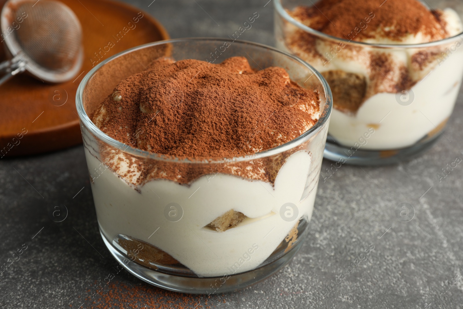 Photo of Delicious tiramisu in glass on grey table